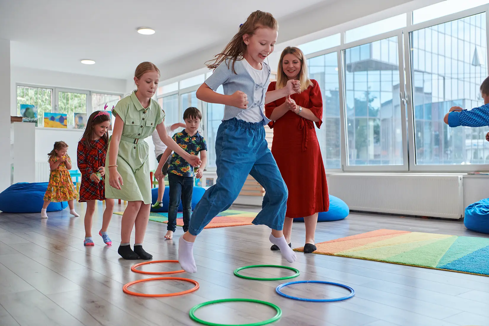 Kinder hüpfen fröhlich in Hula-Hoop-Ringe im Sport- und Spielkurs, Sportlehrerin ist begeistert